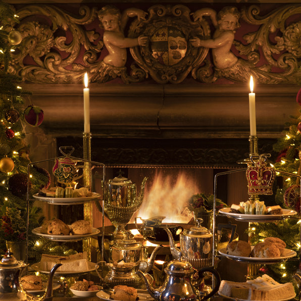 Festive Christmas afternoon tea at Prestonfield House, Edinburgh, with tiered stands of seasonal sandwiches, scones and cakes displayed by a glowing open fire, surrounded by candlelight and Christmas decorations